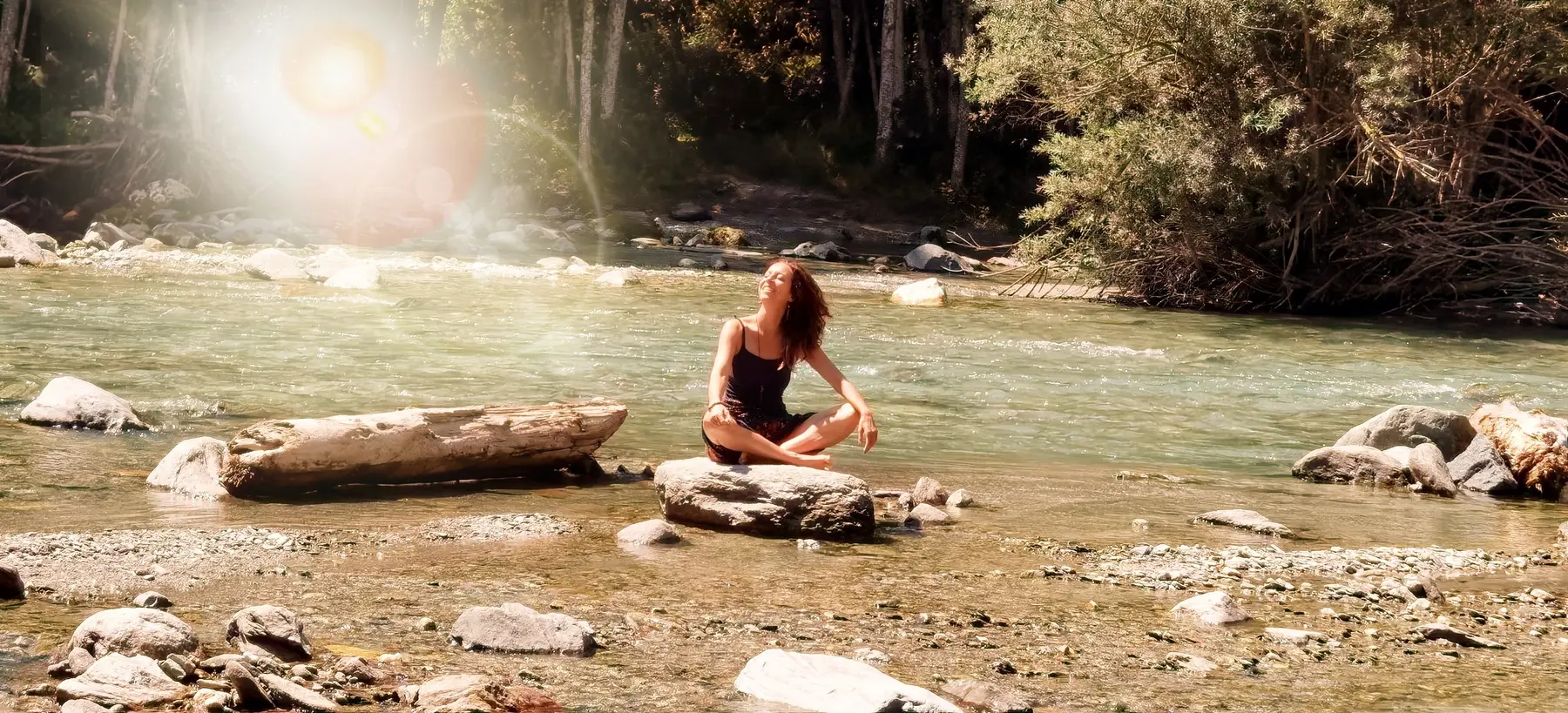 Emilie Burget assise en méditation sur un rocher, au bord d’une rivière